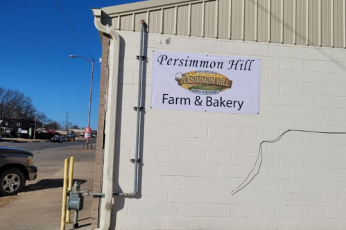 Sign on a building reading "Persimmon Hill Farm & Bakery," with a clear blue sky in the background.